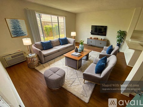 A living room with a grey couch, a grey armchair, a grey ottoman, a wooden coffee table, a flat screen TV, a plant, and a painting of a tree.