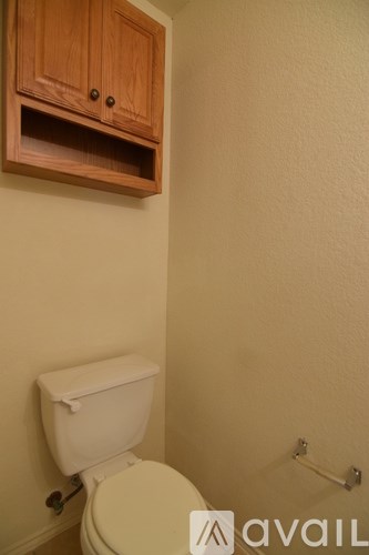 A white toilet in a small bathroom with a wooden cabinet above it.