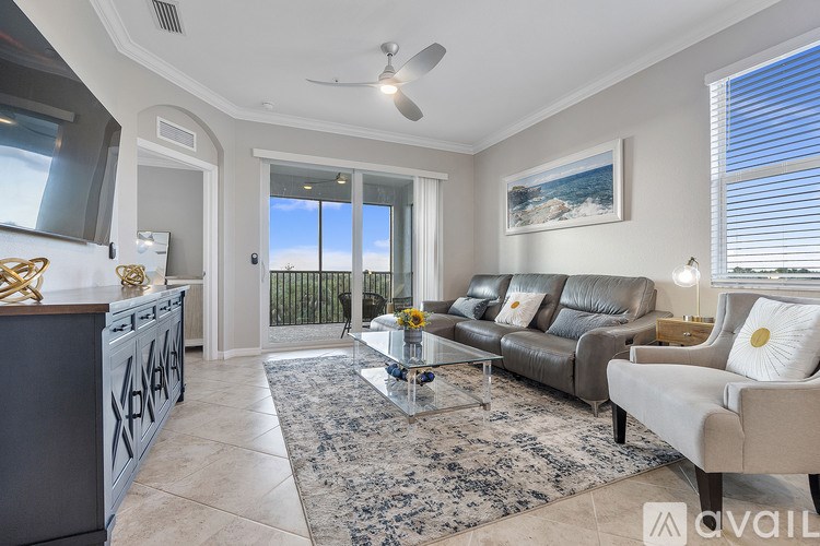 A living room with a grey sofa, a glass coffee table, and a ceiling fan.