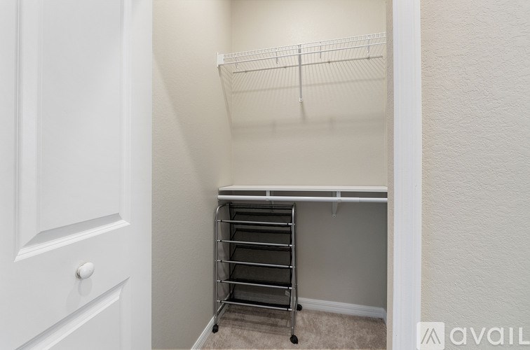 A white door is on the left of a hallway with a metal rack on the right.