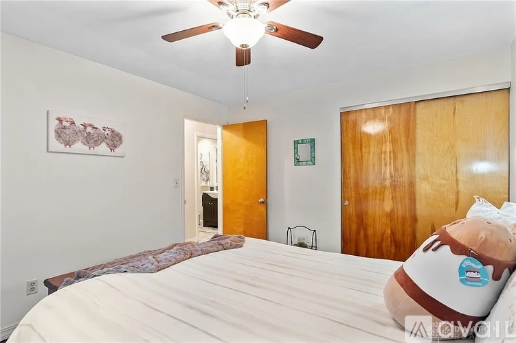 A bedroom with a bed, a ceiling fan, and a painting on the wall.