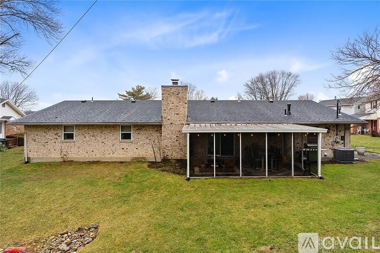 A house with a stone wall and a chimney is surrounded by a grassy yard.