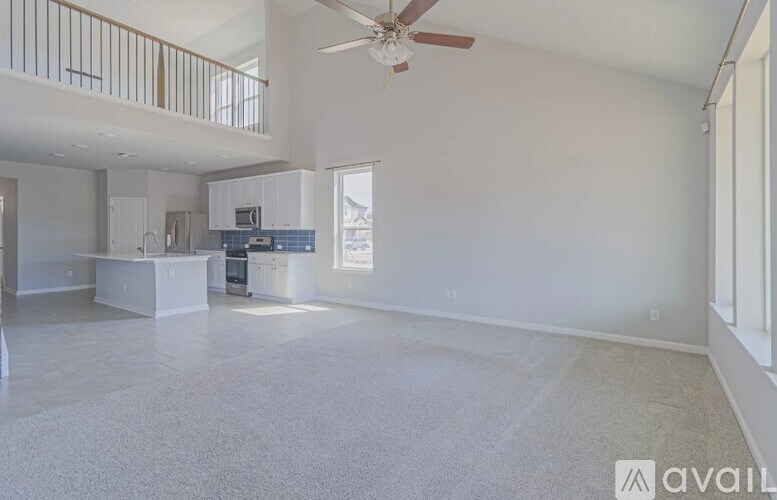 A spacious living room with a ceiling fan and a kitchen area in the background.