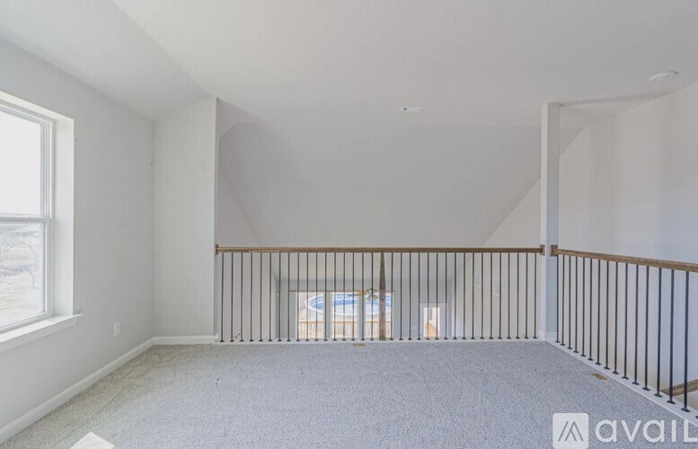 A spacious room with a carpeted floor, a window, and a balcony with a railing.