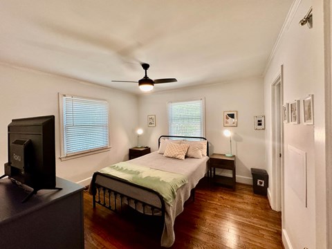 A bedroom with a bed, a television, and a ceiling fan.