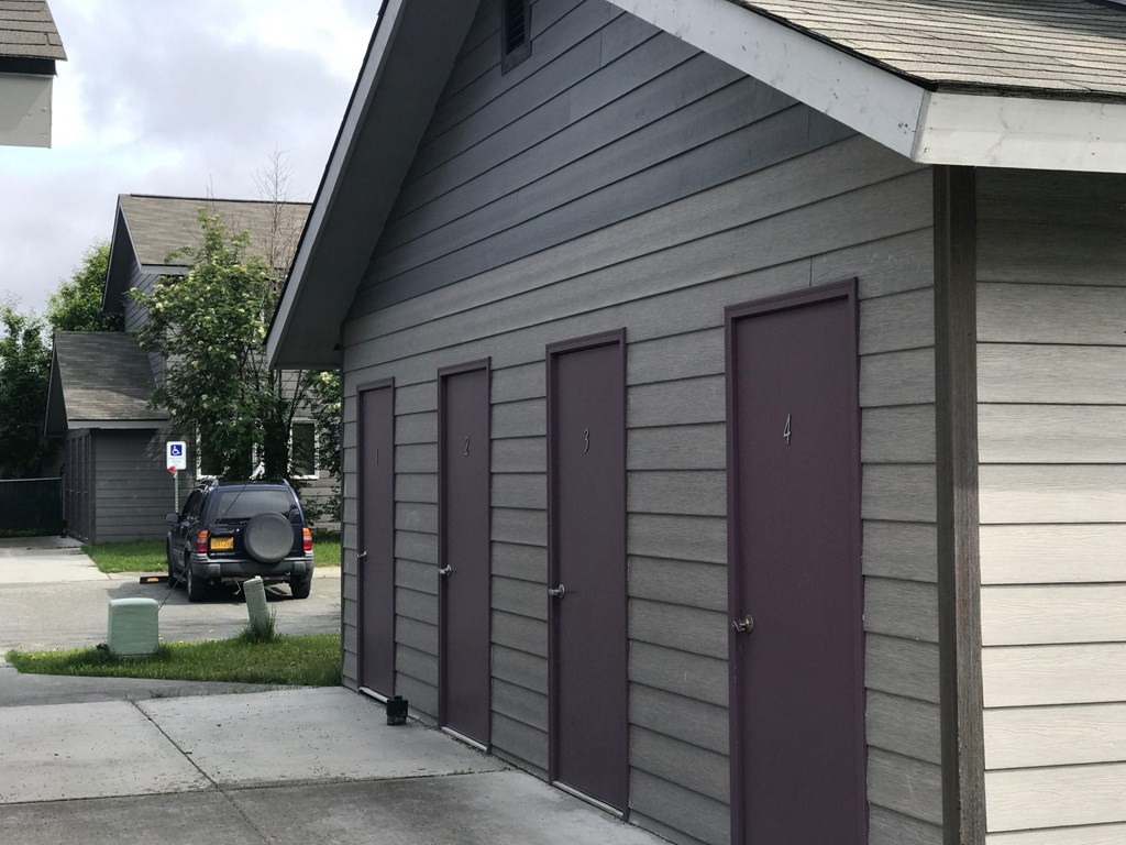 A grey building with a purple door and a black car parked in front.