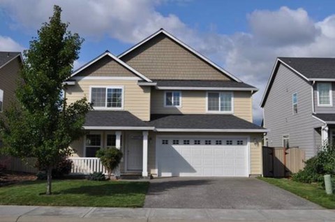 A two-story house with a garage and a tree in front.