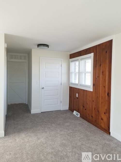 A room with a white door and a window with wooden paneling on the wall.