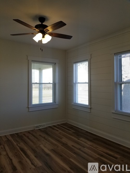 A room with a ceiling fan and two windows.