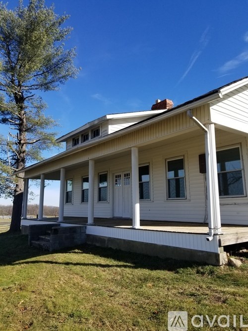 A white house with a porch and a tree in front.