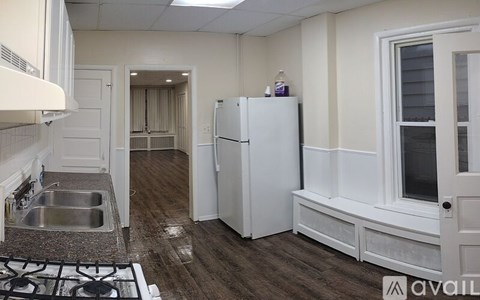A white doorway opens to a kitchen with white cabinets and a green backsplash.