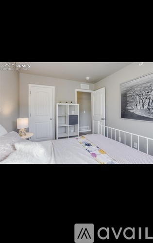 A bedroom with a bed, a nightstand with a lamp, a bookshelf, and a framed picture on the wall.