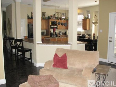 A living room with a tan couch and a kitchen in the background.