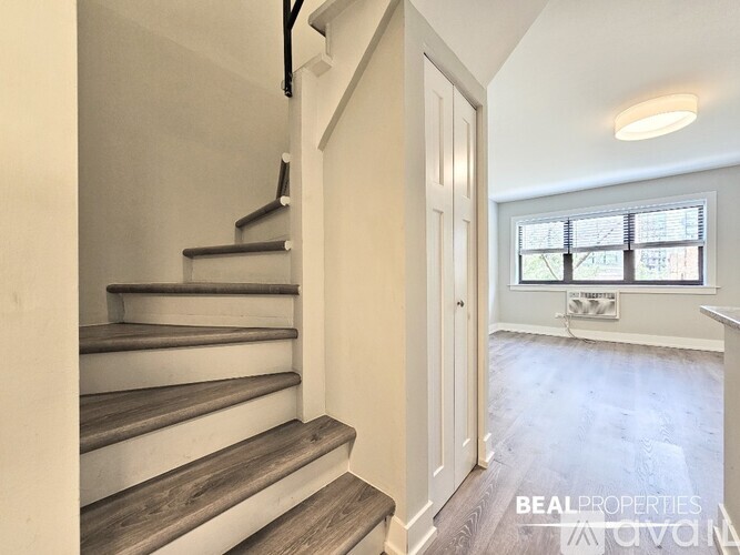 A spacious room with wooden flooring and a window with blinds.