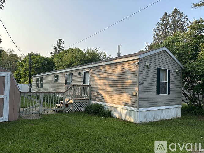 A mobile home with a deck and a small shed in the backyard.