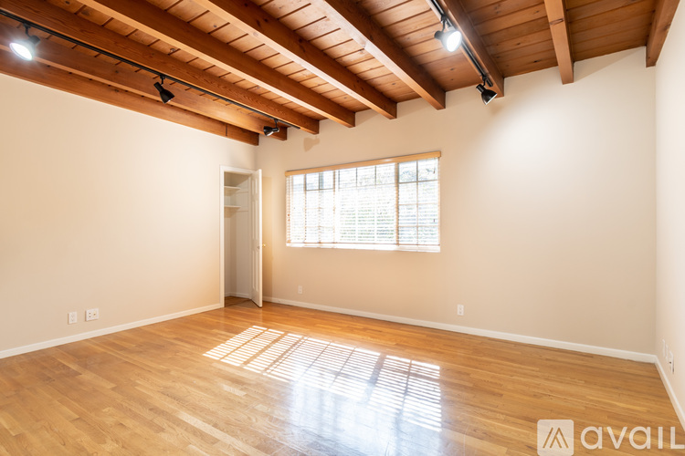 A spacious room with wooden floors and a window with blinds.