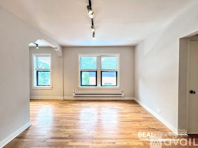 A room with wooden floors and two windows with blinds.