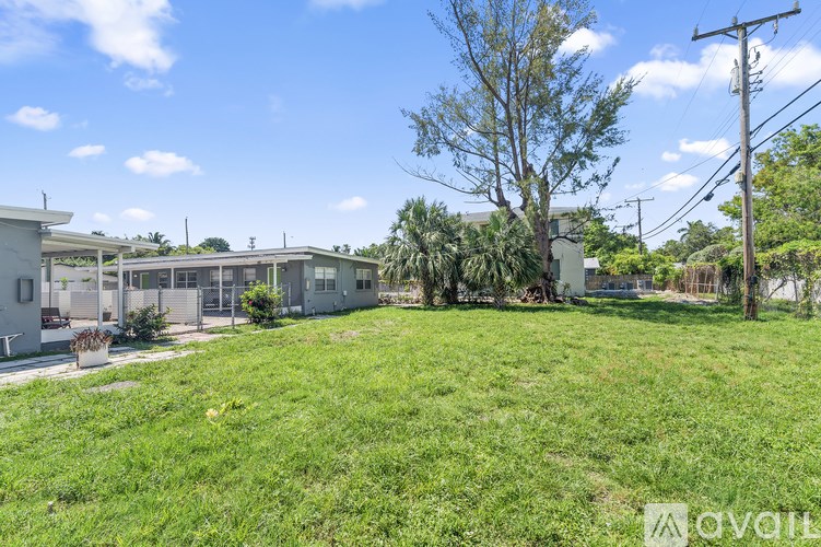 A grassy area with a building in the background and a tree in the foreground.