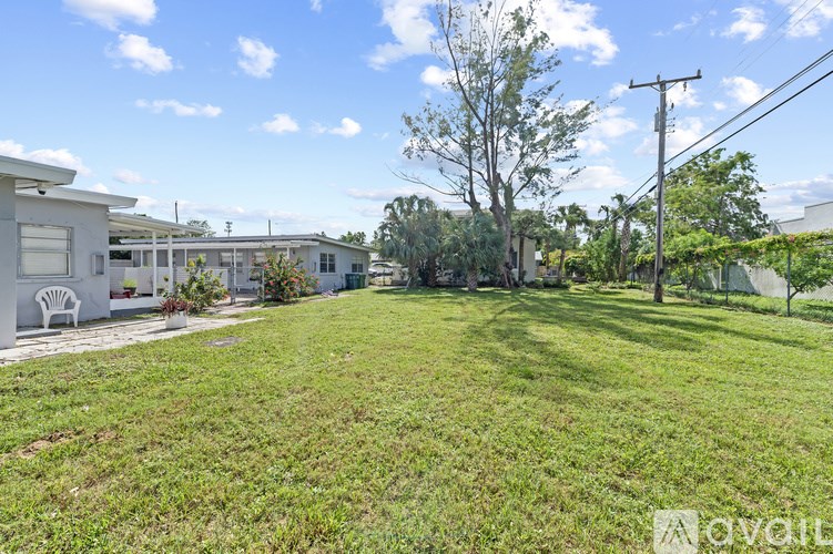A red car is parked in a parking lot with two grey buildings in the background.