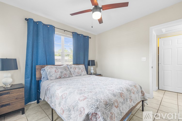 A bedroom with a bed, blue curtains, and a ceiling fan.