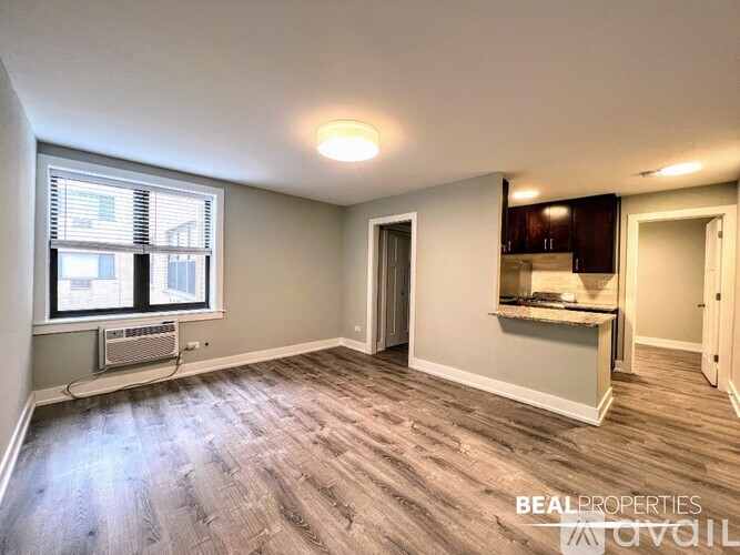 A spacious empty room with wood flooring and a window with blinds.