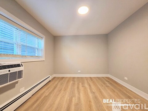 A spacious room with wooden flooring and a large window.
