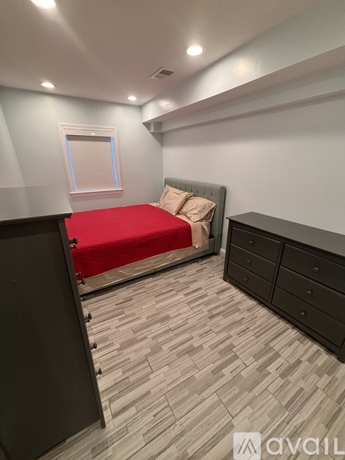 A bedroom with a red bedspread and a grey headboard.