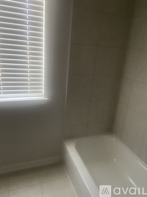 A white tiled bathroom with a window and a bathtub.