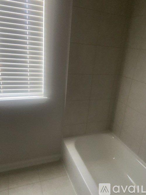 A white tiled bathroom with a window and a bathtub.