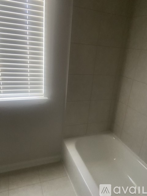 A white tiled bathroom with a window and a bathtub.