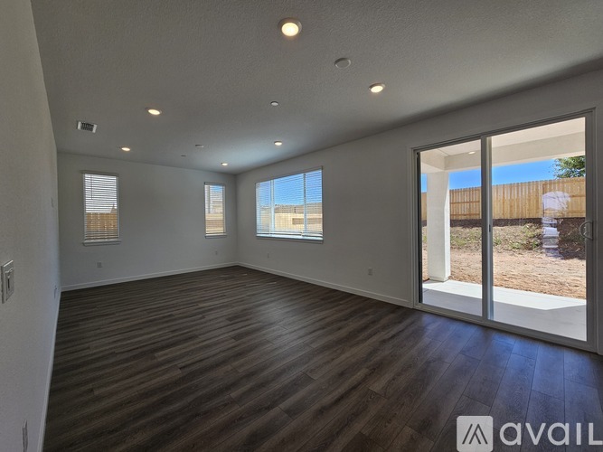 A spacious room with wooden floors and sliding glass doors leading to a backyard.