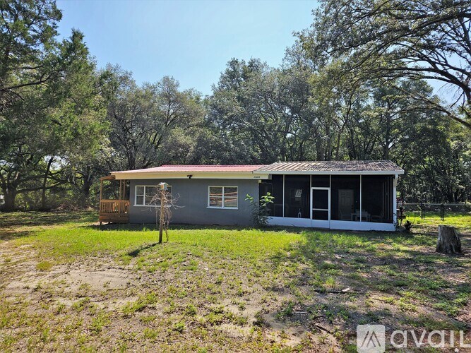 A house with a grey roof and white walls is surrounded by trees.