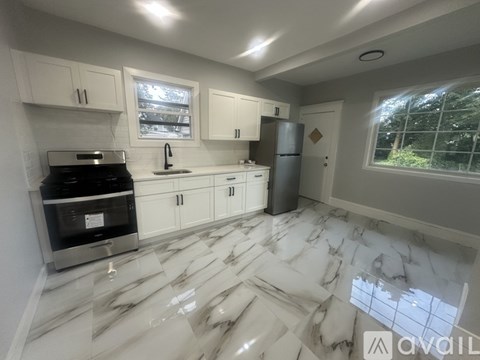 A kitchen with white cabinets and marble flooring.
