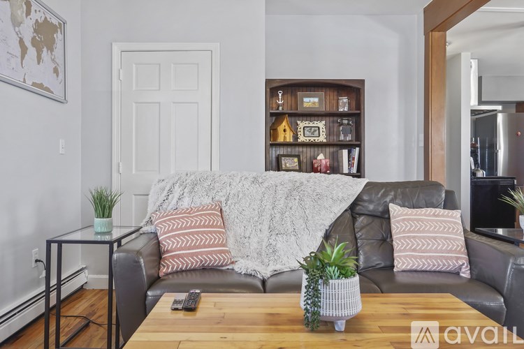 A living room with a grey couch, a coffee table, and a wooden shelf with various decorative items.