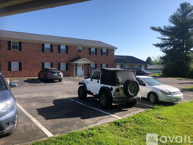 A white car is parked in a parking lot in front of a brick building.