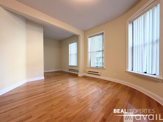 A room with wooden flooring and two windows with white curtains.