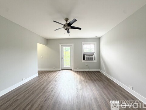 A spacious room with a ceiling fan and hardwood flooring.