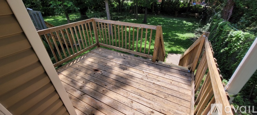 A wooden deck with a railing and steps leading to a grassy area.