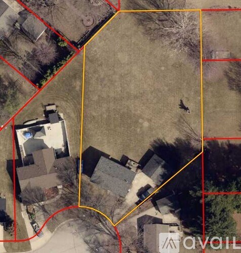 A bird is flying over a field with a house and trees in the background.