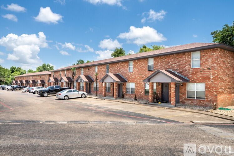 A row of red brick houses with cars parked in front.