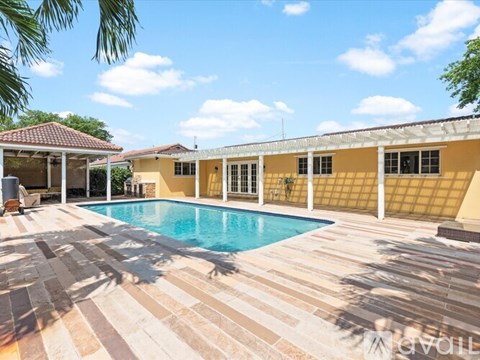 A pool surrounded by a tiled patio and a yellow building.