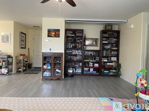 A living room with a large bookshelf filled with books and a ceiling fan.