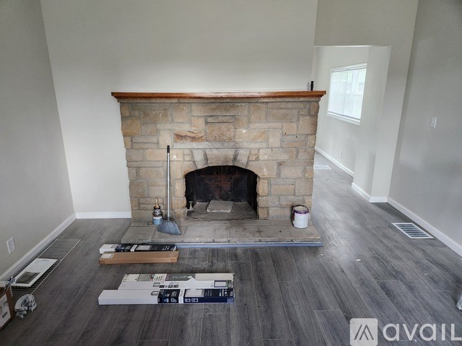 A stone fireplace with a wood burning stove in the middle of a room with wooden floors.