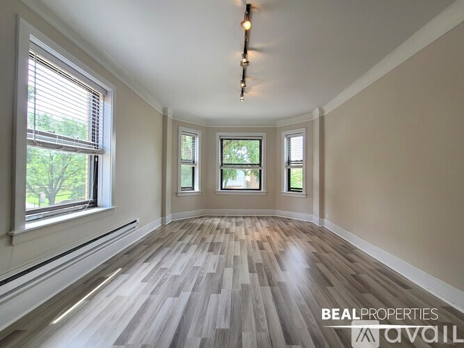 A room with wooden flooring and three windows.