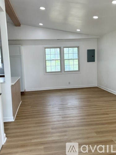 A room with wooden flooring and two windows.