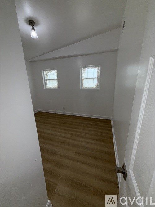 A room with wooden flooring and two windows.