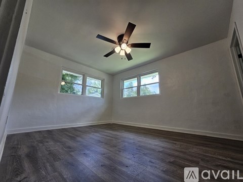 A room with a ceiling fan and two windows.
