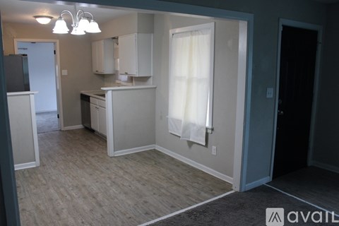 A kitchen area with a refrigerator, cabinets, and a window with curtains.
