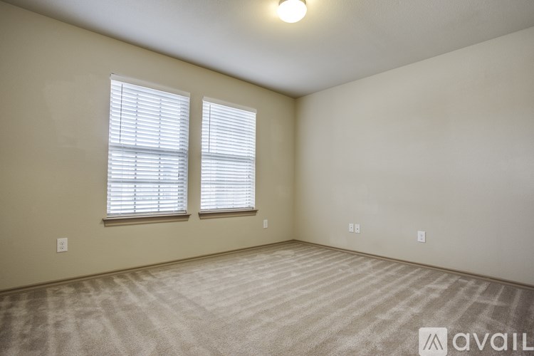 A room with a carpeted floor and two windows with blinds.
