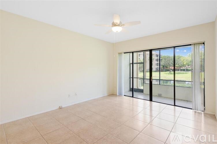 A spacious room with a ceiling fan and sliding glass doors leading to a balcony.